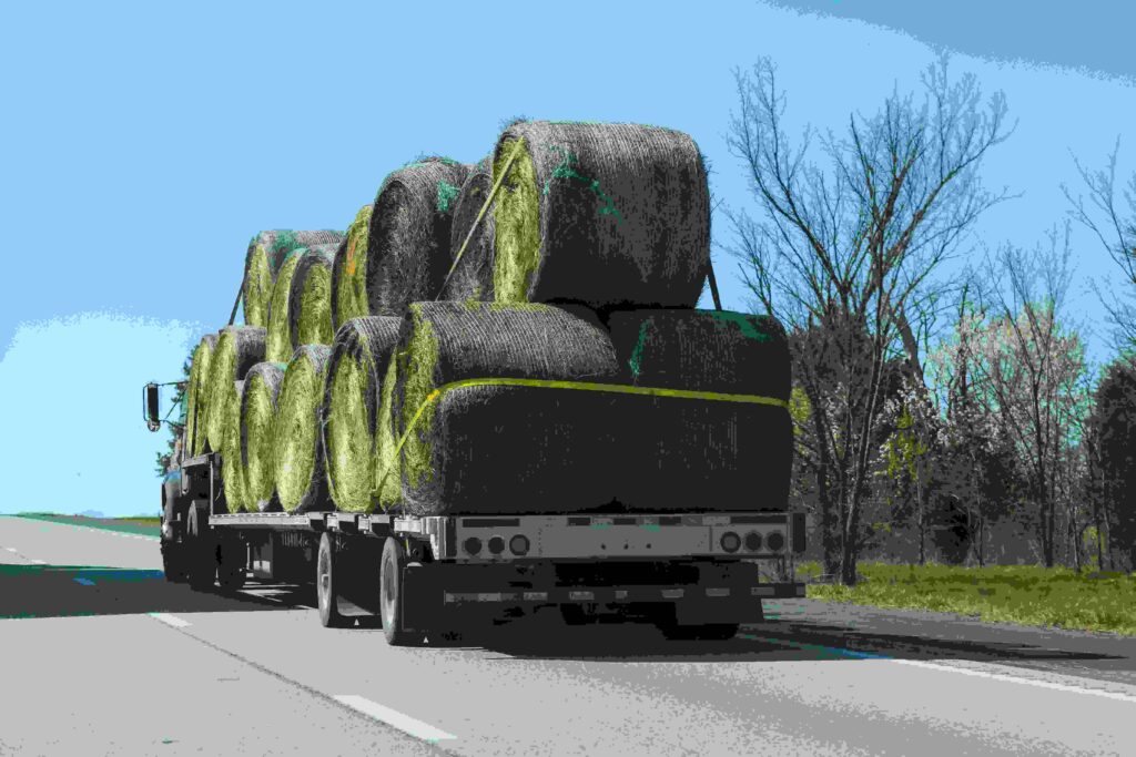 Flatbed truck hauling stacked hay bales on a highway